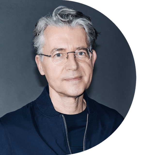Matthias Schrader ist ein Mann mit hellgrauen, mittellangen Haaren und schmaler Brille. Er lächelt in die Kamera und trägt eine dunkelblaue Jacke